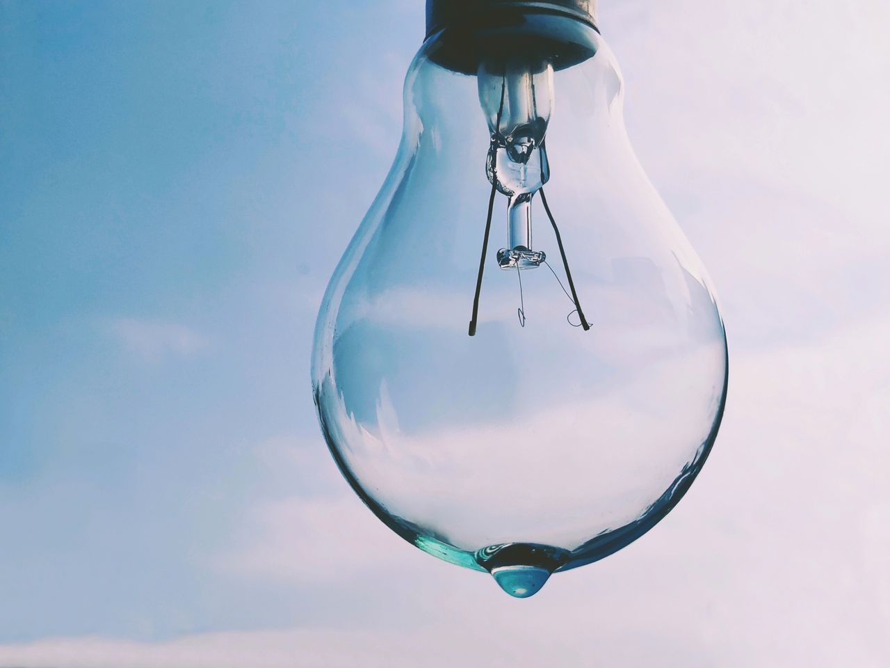 A close-up photo of a clear light bulb against a bright blue sky background.